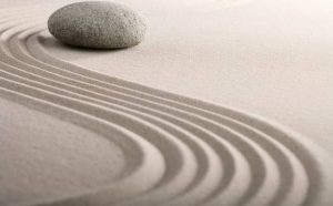 Une pierre repose sur le sable avec un motif de vagues. La question "Pourquoi rêver de sable en islam ?" est posée